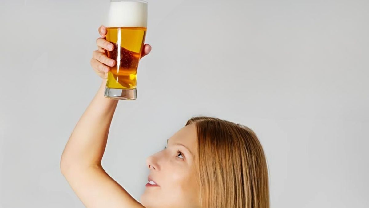 Người giơ cao ly bia đầy bọt, nhìn lên, nền trắng.