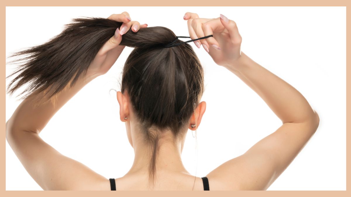 Người đang buộc tóc đuôi ngựa cao bằng dây buộc tóc màu đen, nền trắng.