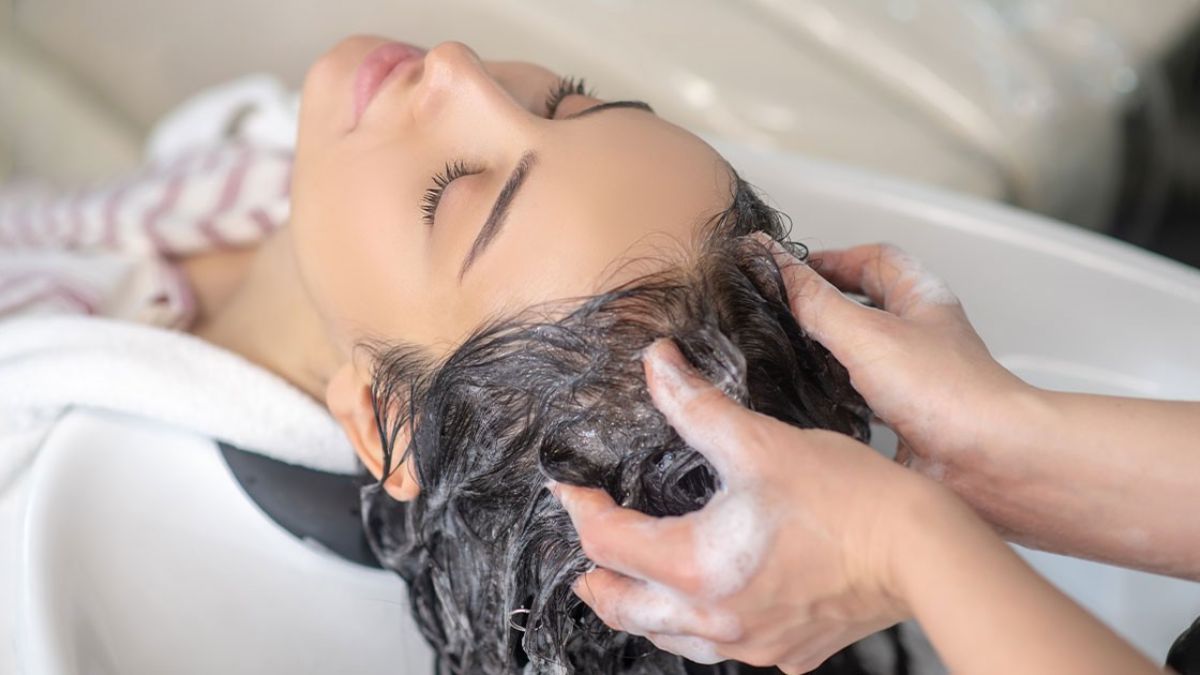Người đang được gội đầu tại tiệm, với bàn tay đang massage và tạo bọt trên tóc.