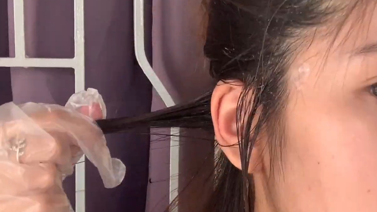 Người đang nhuộm tóc, tay đeo găng tay nhựa, với một lọn tóc được kéo ra gần tai.