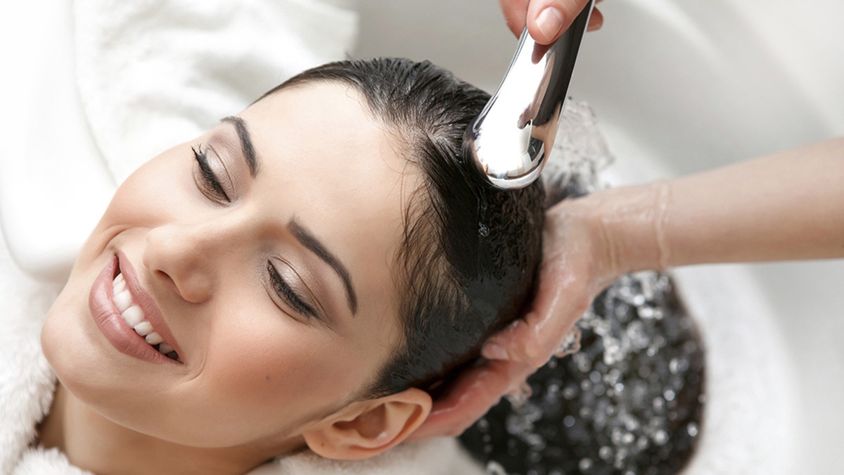 Người phụ nữ đang được gội đầu tại salon, nước chảy từ vòi sen trên đầu cô.
