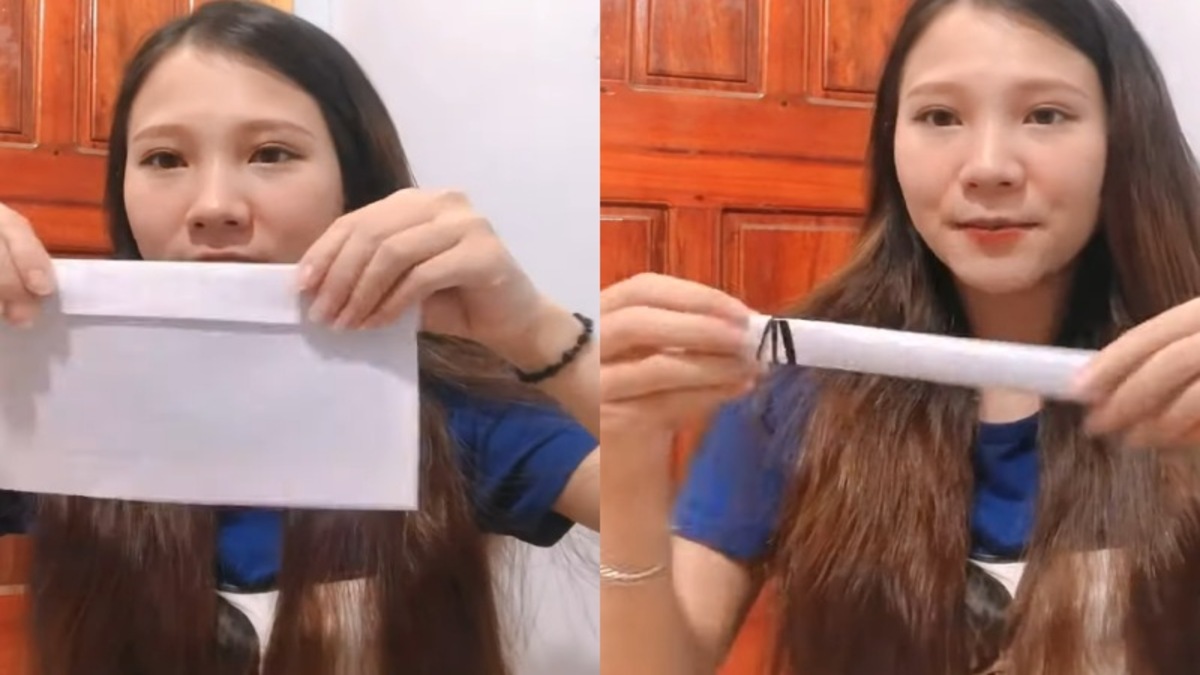 Người phụ nữ cầm phong bì trắng và giấy cuộn, đứng trước cửa gỗ.