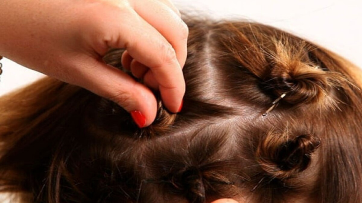 Người đang tạo kiểu tóc với các lọn tóc nhỏ được ghim lại trên đầu, tay cầm một lọn tóc.