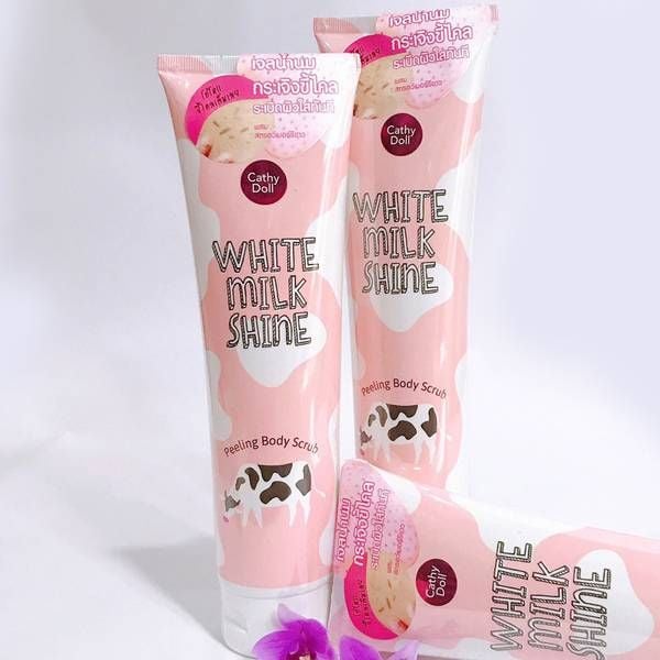 cathy_doll_white_milk_shine_peeling_body_scrub_345489a1ed5e4e9ba478ee8e52395ca6_grande Ba tuýp tẩy tế bào chết có thiết kế màu hồng trắng, nhãn "White Milk Shine", xếp trên nền trắng với hoa tím.