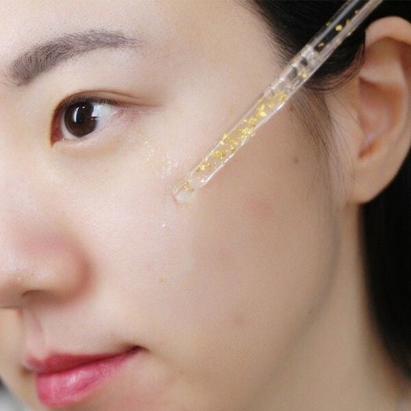 cham_soc_lan_da_cua_ban_voi_tinh_chat_vang_24k_77c76de47e1b40d48f11c889a7a1b7e0_grande Người đang sử dụng ống nhỏ giọt để thoa serum lên da mặt, tập trung vào vùng má.