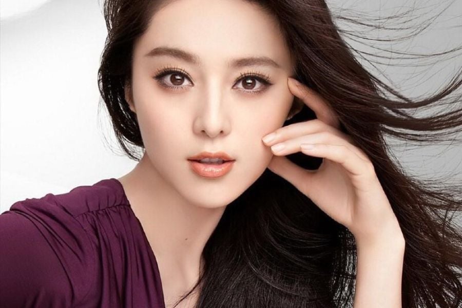 Người phụ nữ tóc dài, mặc áo tím, nhìn thẳng vào máy ảnh với tay đặt nhẹ lên mặt.