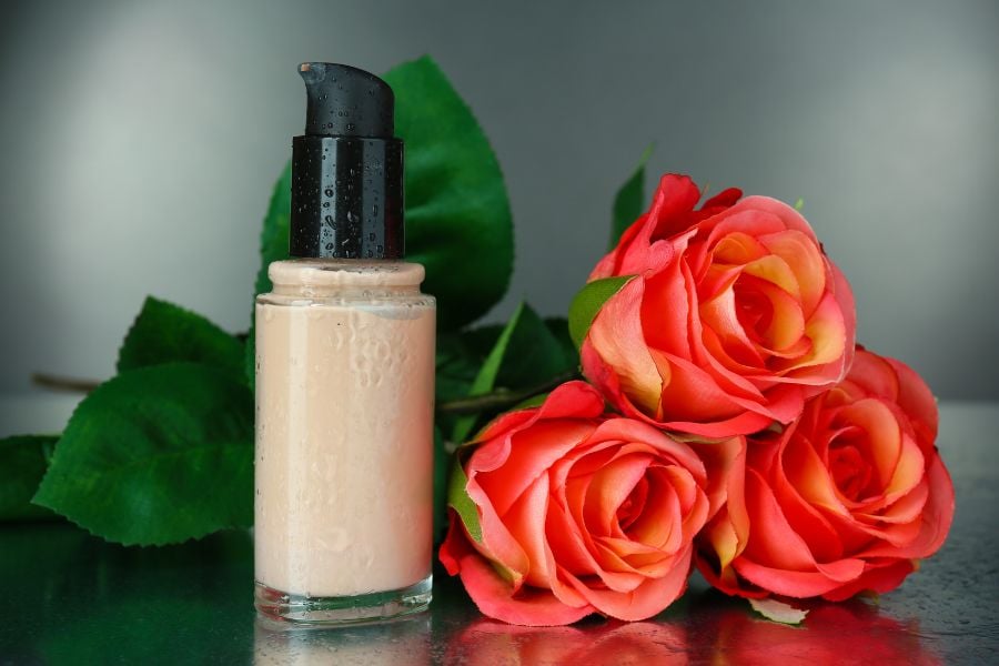 Chai lọ mỹ phẩm với bơm màu đen đặt cạnh hoa hồng đỏ trên nền xám.