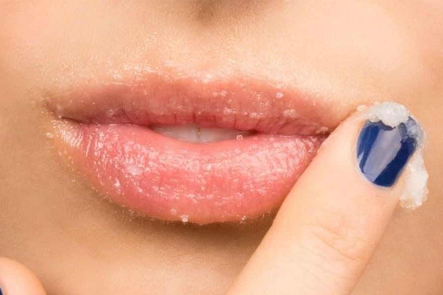 Đôi môi đang được tẩy tế bào chết bằng tay có sơn móng tay màu xanh.