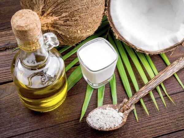 Dầu dừa trong chai, nửa quả dừa, ly sữa dừa và thìa dừa nạo trên nền lá xanh.