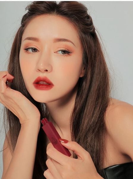 Người phụ nữ cầm son môi màu đỏ, trang điểm kỹ lưỡng, nhìn xa xăm.