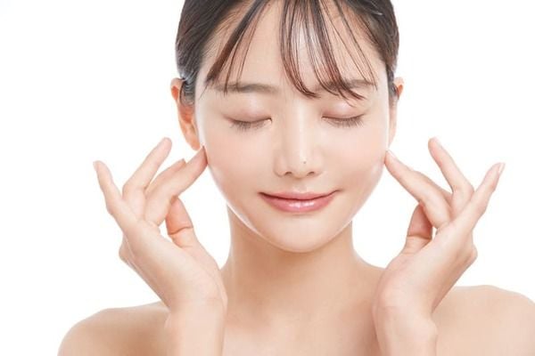 Người phụ nữ nhắm mắt, mỉm cười nhẹ nhàng, đặt tay lên má trên nền trắng.