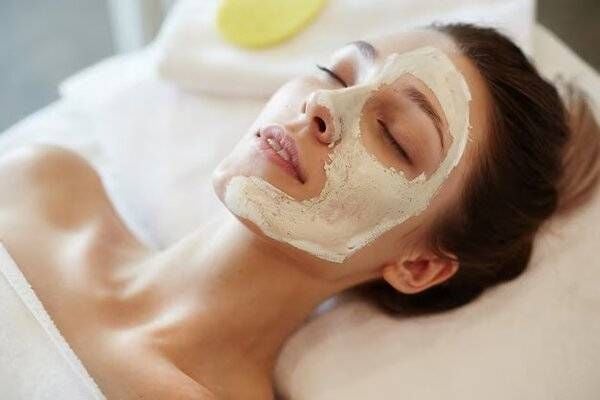 Người đang thư giãn với mặt nạ dưỡng da trên mặt, nằm trên giường spa, mắt nhắm.