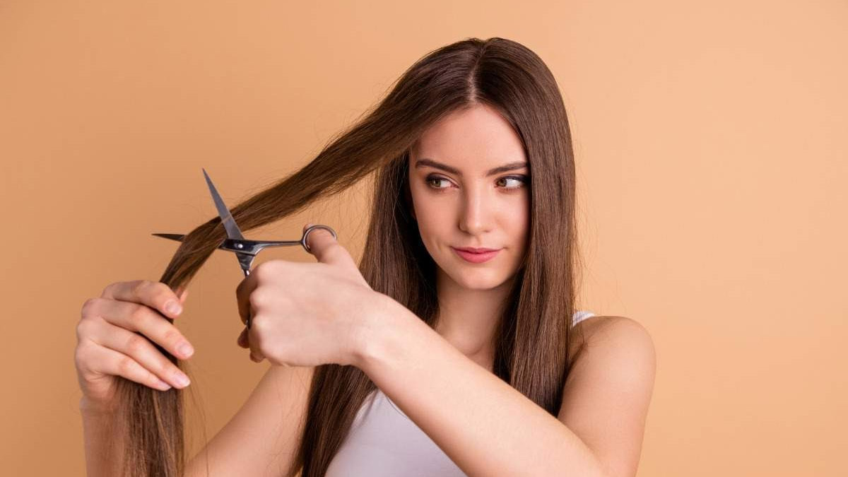 dau-nam-co-nen-cat-toc-2 Người cầm kéo tự cắt tóc dài, nền màu cam nhạt.