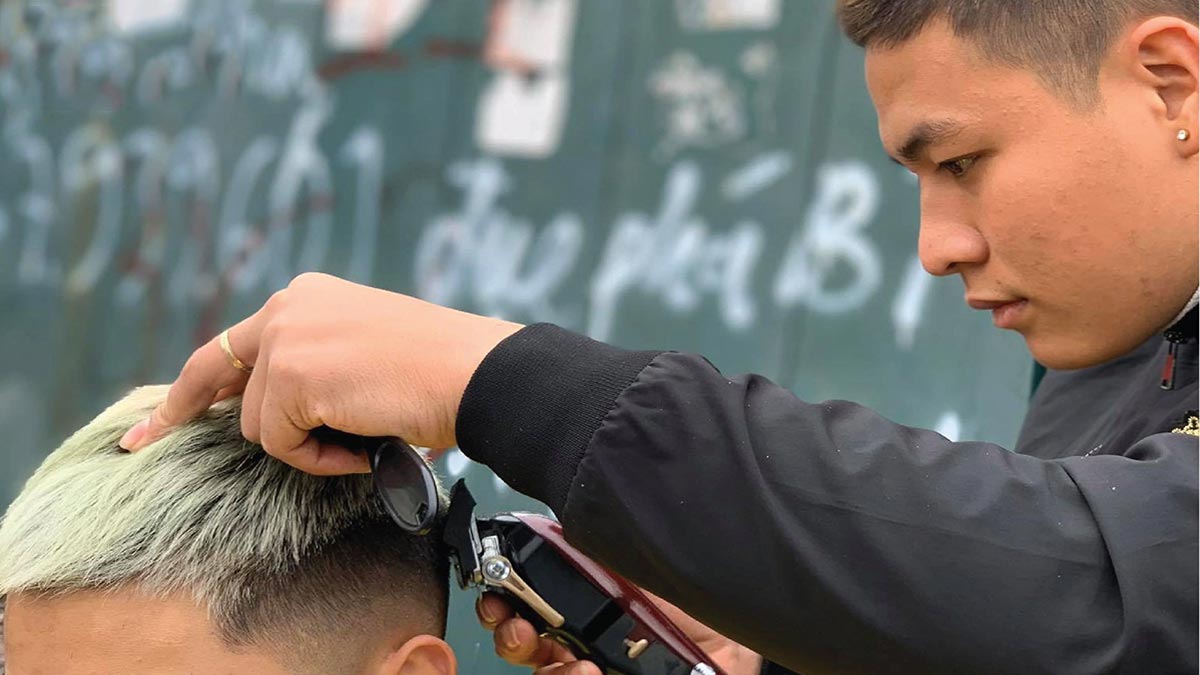 dau-nam-co-nen-cat-toc-4 Người thợ cắt tóc đang tỉa tóc cho khách hàng với tông đơ, nền phía sau có tường vẽ graffiti.