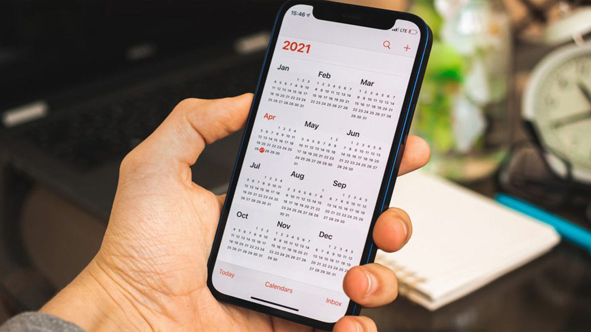 dau-nam-co-nen-cat-toc-7 Người cầm điện thoại hiển thị lịch năm 2021, xung quanh là máy tính và đồng hồ bàn.