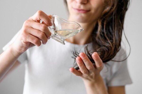 Người cầm ly thủy tinh đổ chất lỏng lên tay và thoa lên tóc, mặc áo trắng.