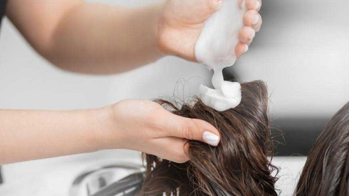 Bàn tay đang thoa kem dưỡng lên tóc ướt, chuẩn bị cho việc chăm sóc tóc trong tiệm làm tóc.