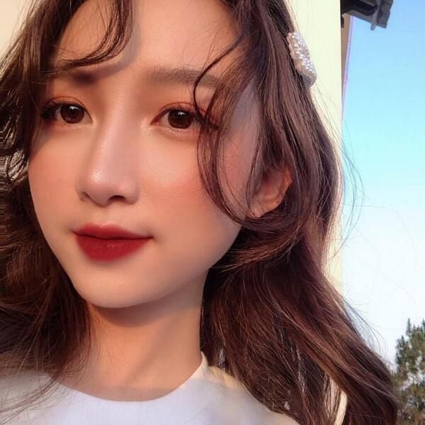 Người phụ nữ chụp cận mặt, tóc dài, trang điểm nhẹ, ánh sáng tự nhiên chiếu vào.
