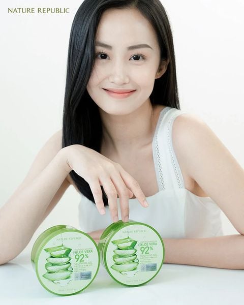 Người phụ nữ mặc áo trắng, cười nhẹ, đặt tay lên hai hộp sản phẩm dưỡng da nha đam Nature Republic.