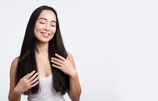 Người phụ nữ trẻ với mái tóc dài, mặc áo trắng, đang mỉm cười nhẹ nhàng trên nền trắng.