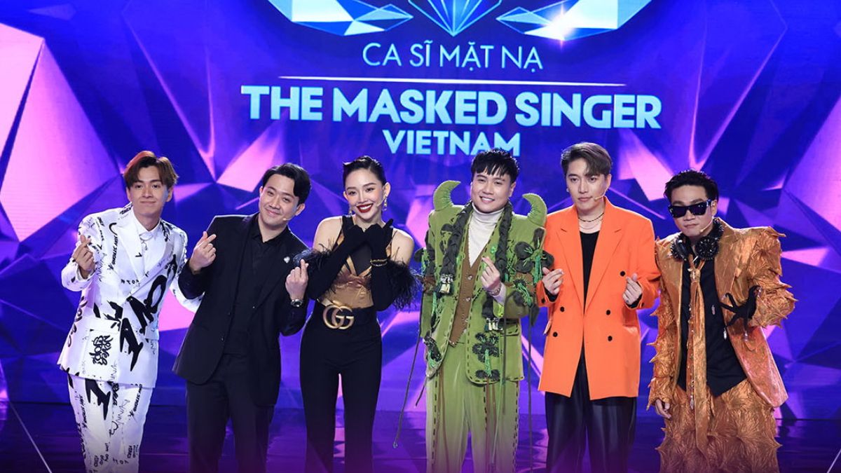 Sáu người đứng trên sân khấu chương trình "The Masked Singer Vietnam" với trang phục đa dạng, nền xanh tím.
