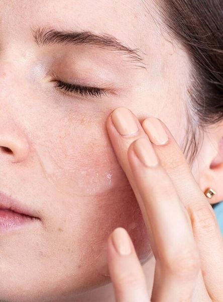 Người đang thoa kem dưỡng lên vùng má, mắt nhắm, thể hiện chăm sóc da mặt.