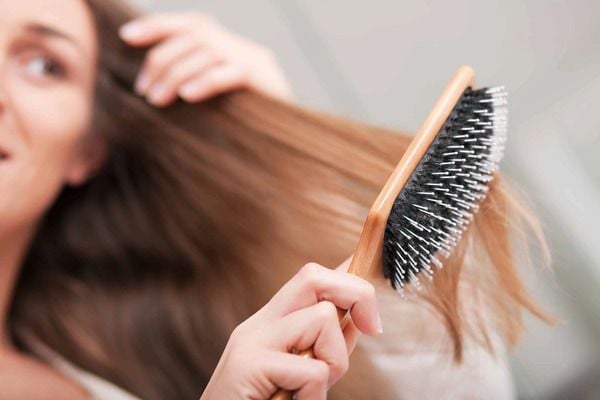 Người đang chải tóc bằng lược, tập trung vào phần tóc và lược gỗ với các răng kim loại.