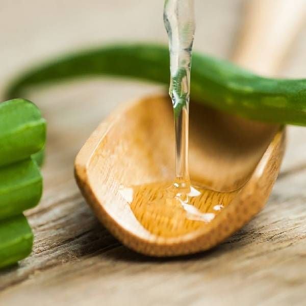Thìa gỗ chứa gel lô hội đang chảy, với lá lô hội xanh bên cạnh trên nền gỗ.