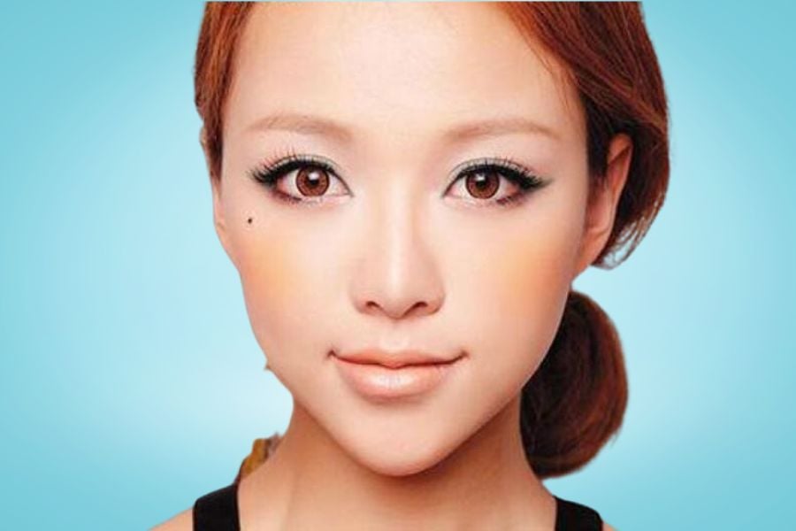Chân dung một người với mái tóc nâu, trang điểm nhẹ, nền xanh dương.