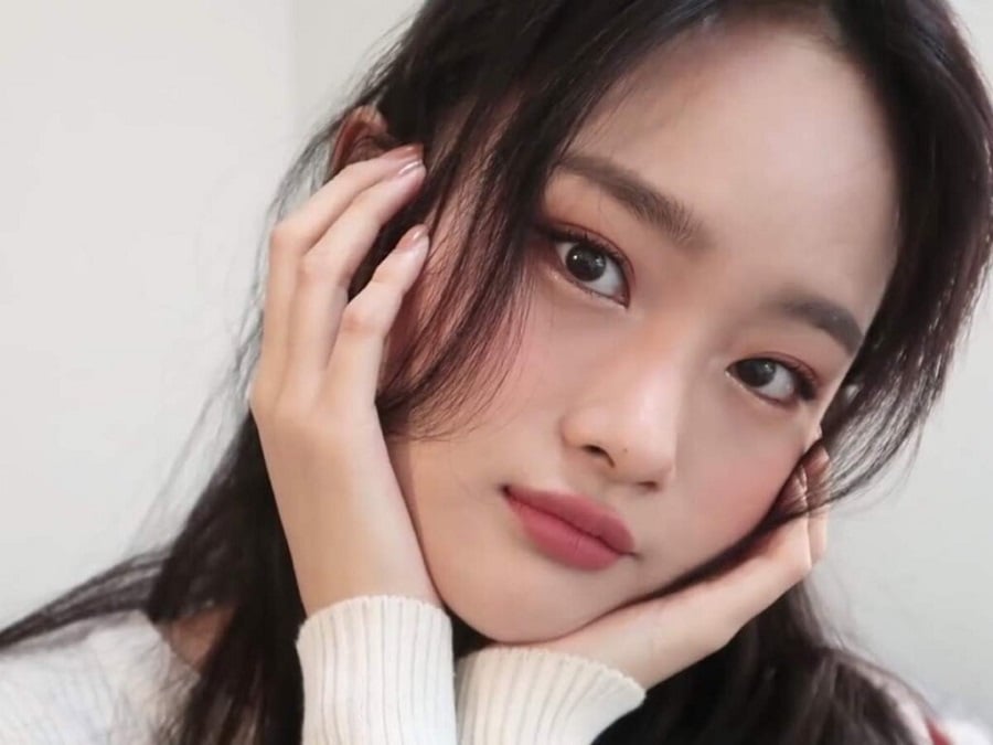 Một người với m&aacute;i t&oacute;c d&agrave;i, chạm tay l&ecirc;n mặt, mặc &aacute;o trắng, nh&igrave;n thẳng v&agrave;o ống k&iacute;nh trong m&ocirc;i trường &aacute;nh s&aacute;ng tự nhi&ecirc;n.