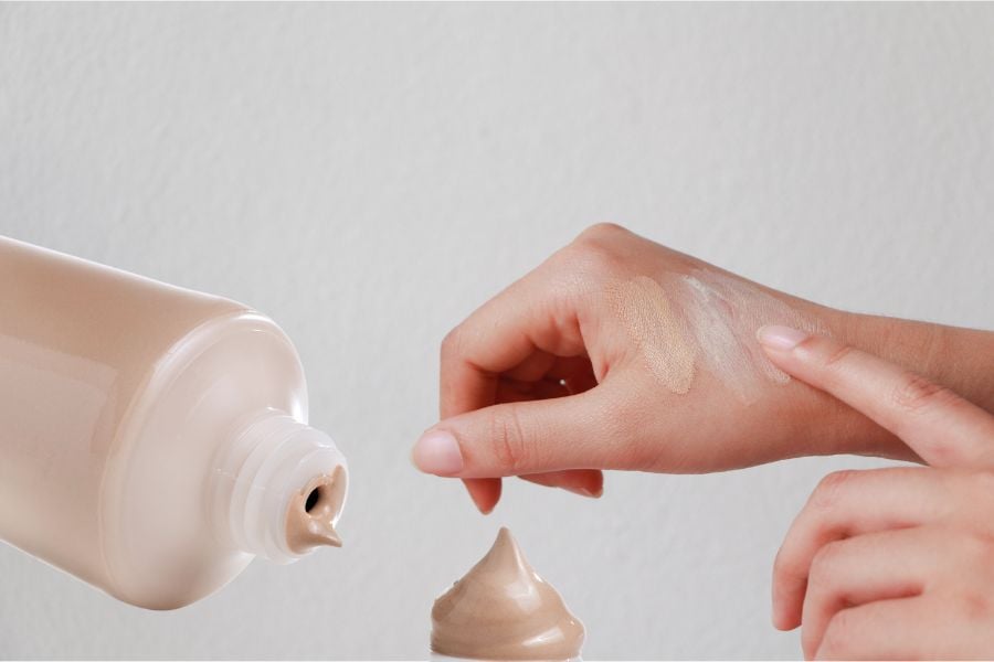 Bàn tay thoa kem nền từ chai, với một ít kem trên da, nền trắng.