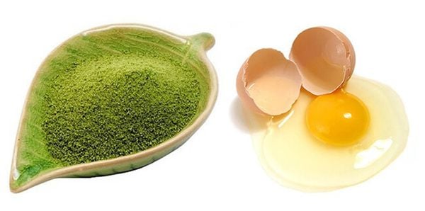 Bột màu xanh trên đĩa lá và trứng gà vỡ với lòng đỏ và lòng trắng trên nền trắng.