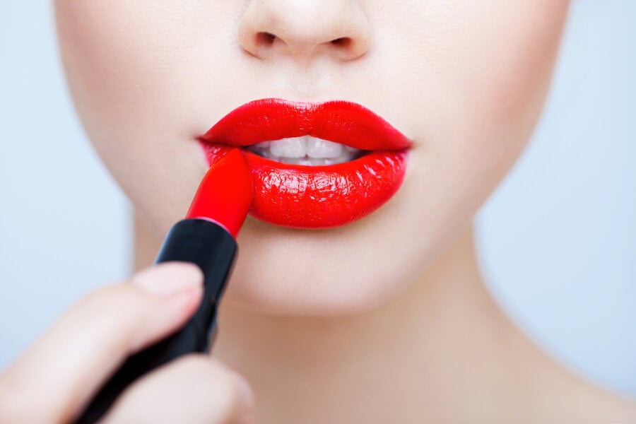 Người đang thoa son đỏ lên môi, cận cảnh đôi môi với màu sắc nổi bật.