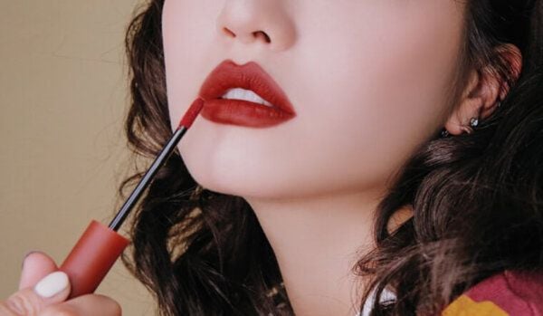 Người đang tô son đỏ lên môi bằng cọ, nền màu trung tính.