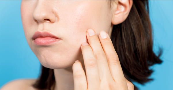 Người phụ nữ chạm vào má, làn da mịn màng, nền xanh dương.