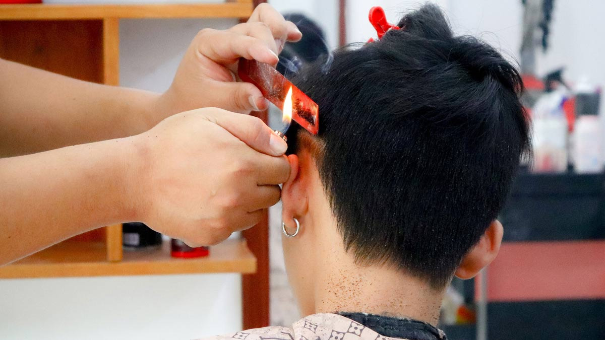 Người thợ cắt tóc đang dùng lửa và lược để tạo kiểu tóc cho khách hàng trong tiệm cắt tóc.