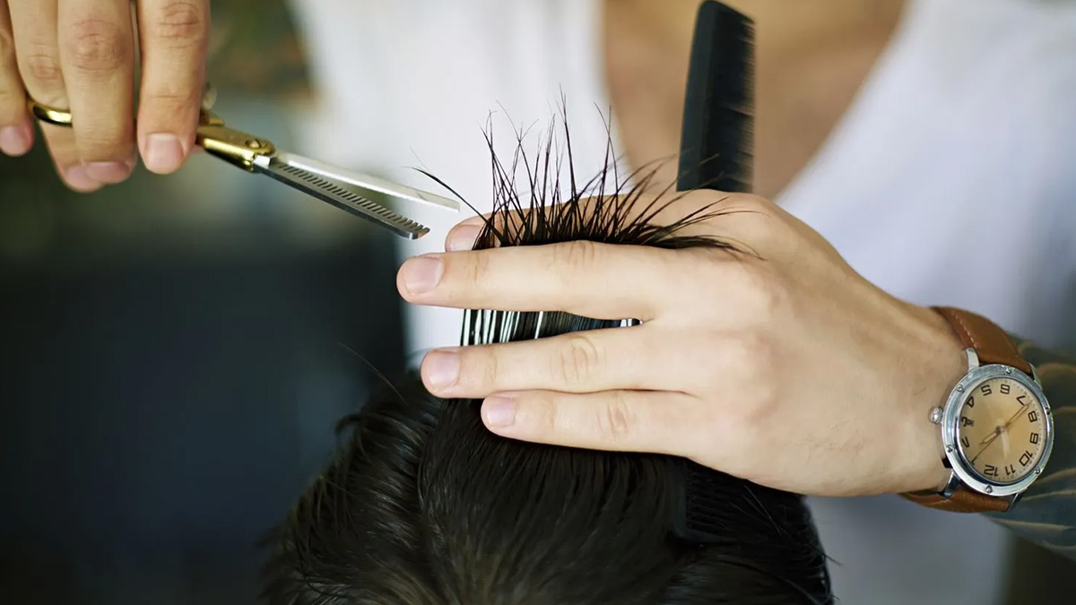 Người đang cắt tóc, tay cầm kéo và lược, tập trung vào cắt tỉa phần tóc phía trên.