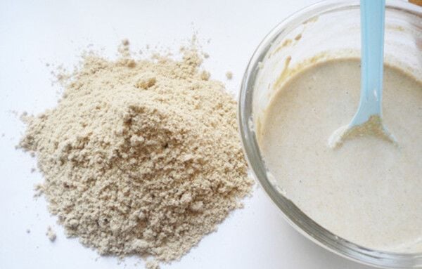Bột và hỗn hợp bột nhão trong bát thủy tinh với muỗng xanh, trên bề mặt trắng.
