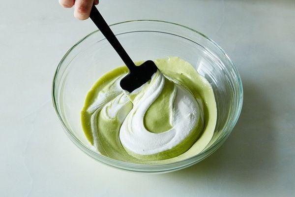 Người đang khuấy hỗn hợp màu xanh và trắng trong tô thủy tinh bằng thìa đen.
