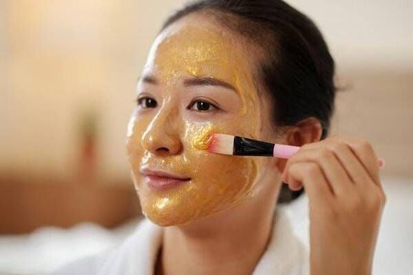 Người đang thoa mặt nạ màu vàng lên mặt bằng cọ trang điểm trong không gian trong nhà.
