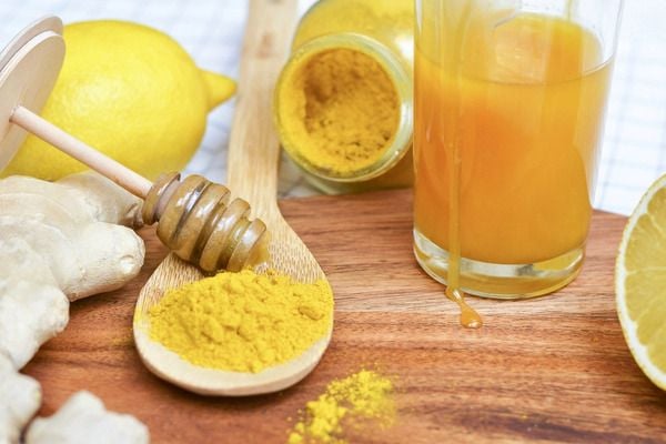 Gừng, chanh, mật ong, bột nghệ và nước cam trên bàn gỗ, tạo nên một bức tranh nguyên liệu tự nhiên.