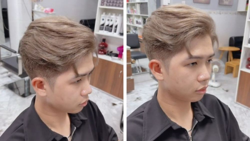 Người mặc áo đen ngồi trong tiệm cắt tóc, tóc nhuộm sáng, phong cách lịch lãm.