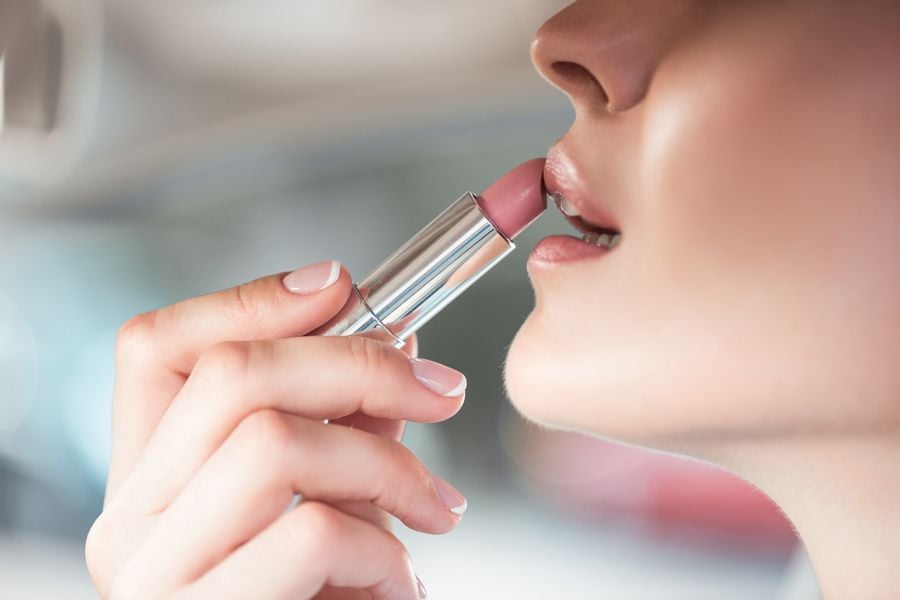 Người đang thoa son môi màu hồng nhạt, cận cảnh khuôn mặt và bàn tay cầm thỏi son.