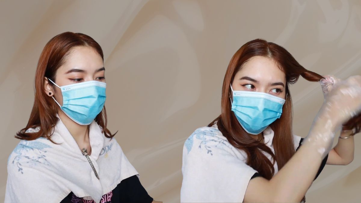 Người đeo khẩu trang xanh, mặc áo bảo vệ, đang tự nhuộm tóc với găng tay nhựa.