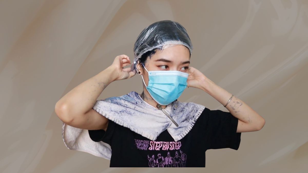 Người đeo khẩu trang xanh, đội mũ nhựa, quàng khăn bảo vệ, đang điều chỉnh mũ.