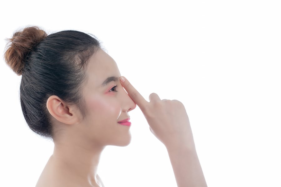 Người phụ nữ nhìn nghiêng, tóc búi, đang đặt ngón tay lên mũi, nền trắng.