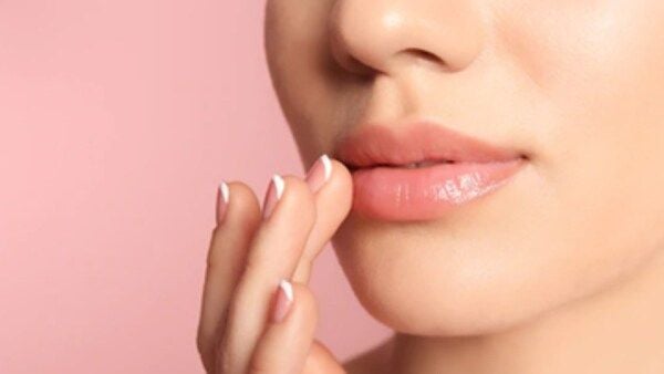Đôi môi hồng nhạt với tay chạm nhẹ, nền hồng nhạt.