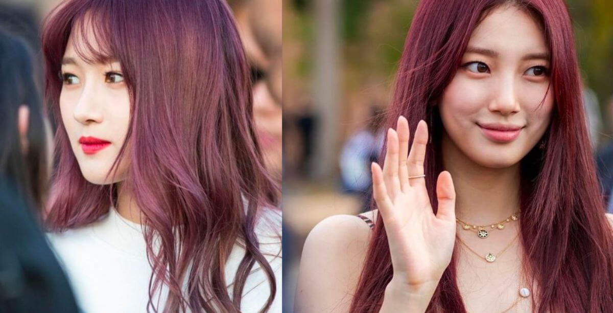 Hai người phụ nữ với mái tóc màu tím đỏ, một người nhìn sang bên, người kia vẫy tay và mỉm cười.