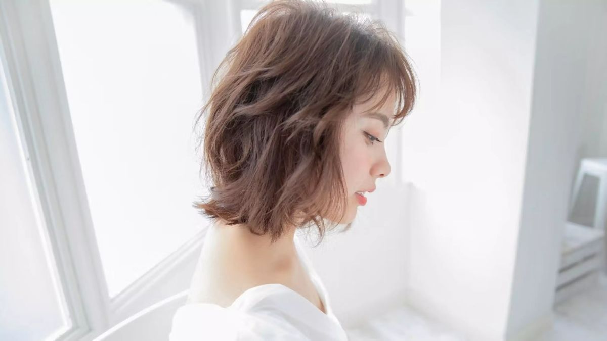 nau-hong-3 Người phụ nữ tóc ngắn đứng nghiêng trong ánh sáng tự nhiên, nền trắng sáng.