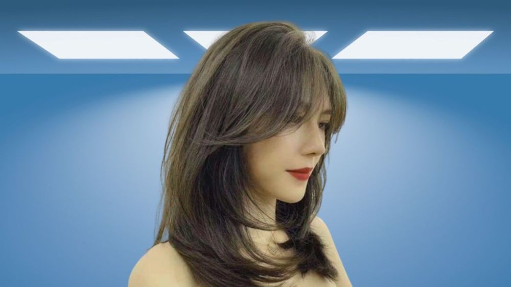 Người phụ nữ với tóc dài, sáng màu đứng trong phòng có ánh sáng đèn trần hình chữ nhật.